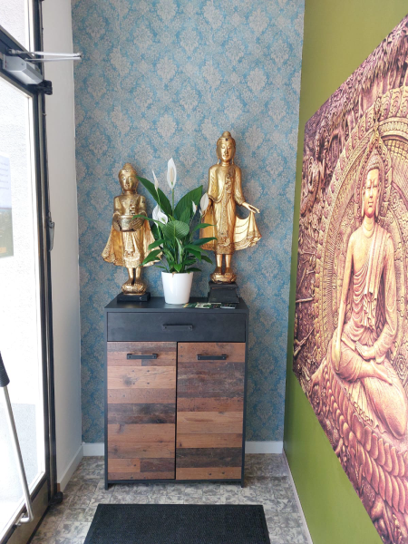 Noi & Tim Traditionelle Thai Massage – Der Eingangsbereich verbindet Tradition und Eleganz: goldene Buddha-Statuen, Pflanzen und kunstvolle Wandgestaltung heißen Sie willkommen.